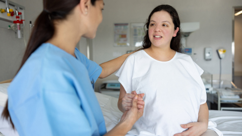 Hebammengeleiteter Kreißsaal / Mutter hält die Hand einer Hebamme, während sie sich auf die Geburt im Krankenhaus vorbereitet